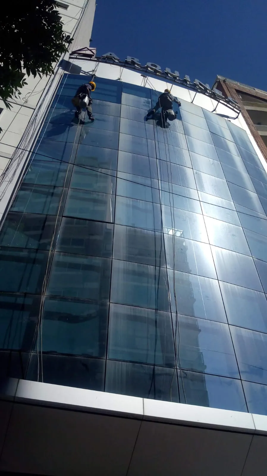 Trabajadores suspendidos frente a un edificio vidriado.
