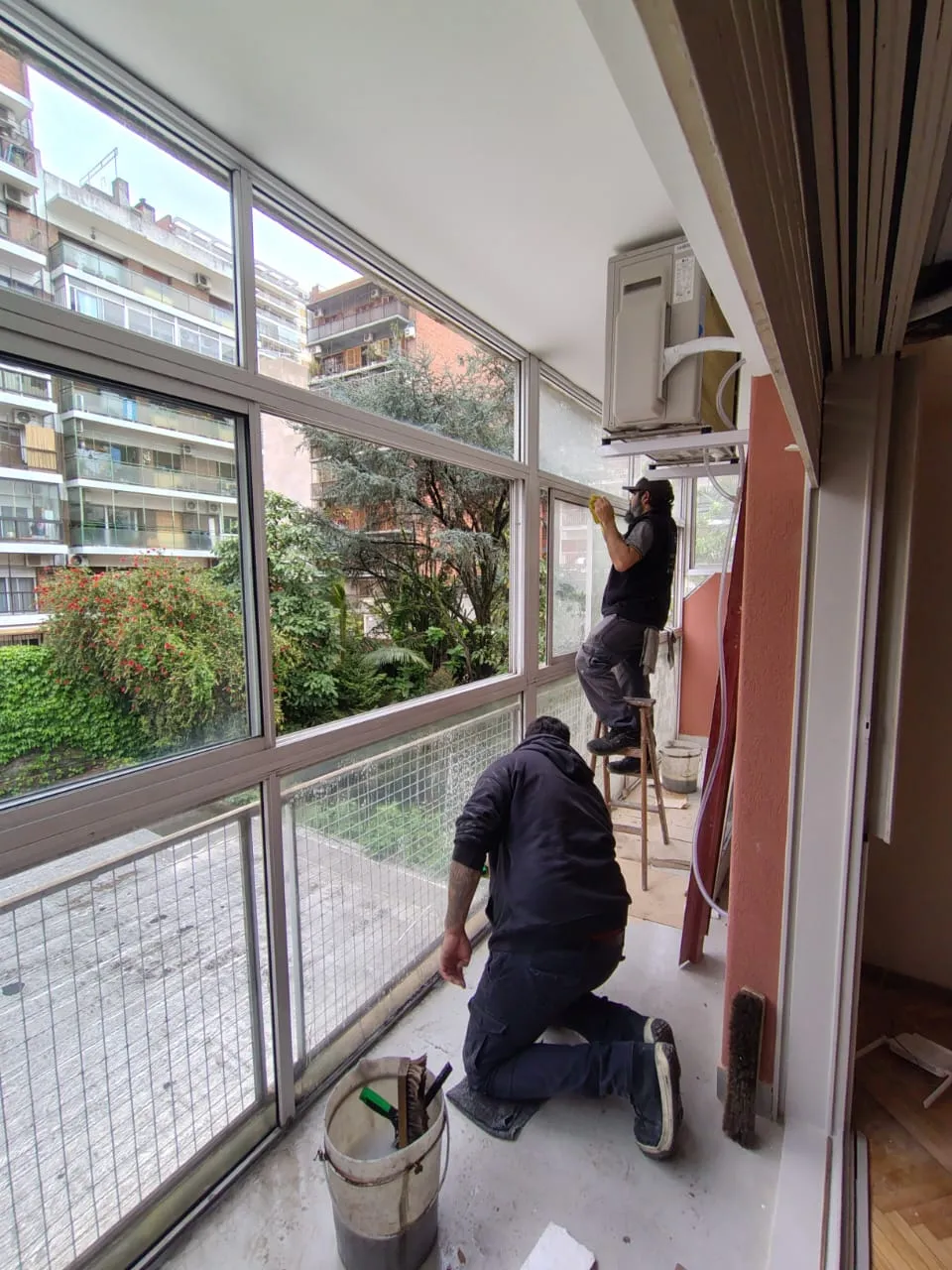 Dos operarios limpiando cristales y carpinterías en una galería interior después de una obra.
