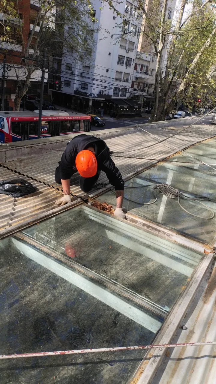 Operario con casco naranja limpiando un paño de vidrio inclinado.