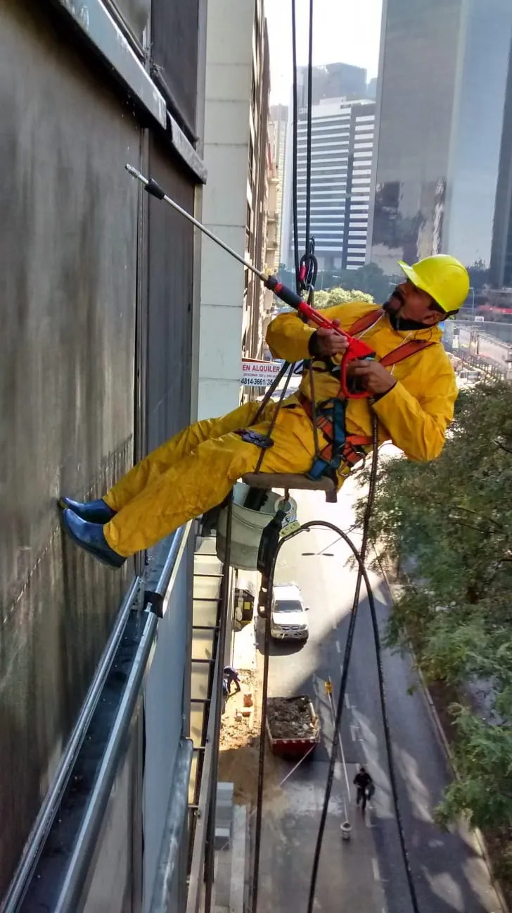 Operario de Agüero con casco amarillo y arnés trabajando mediante cuerdas en una fachada.