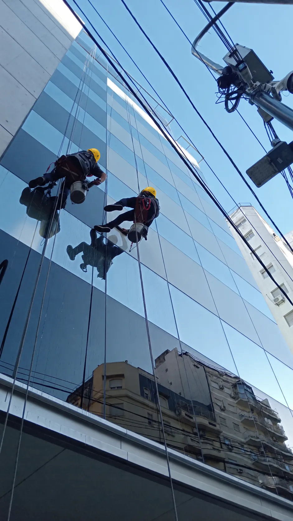 Dos trabajadores con cuerdas frente a una fachada de vidrio.
